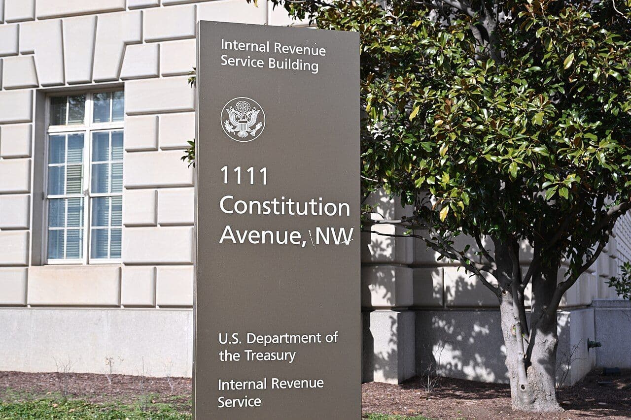 A United States flag flying in front of the columned stone facade of a neoclassical federal government building