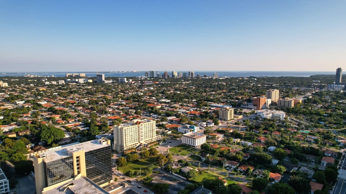 Aerial view of a South Miami neighbourhood of low houses and mid-rise buildings stretching to the bay under a clear blue sky