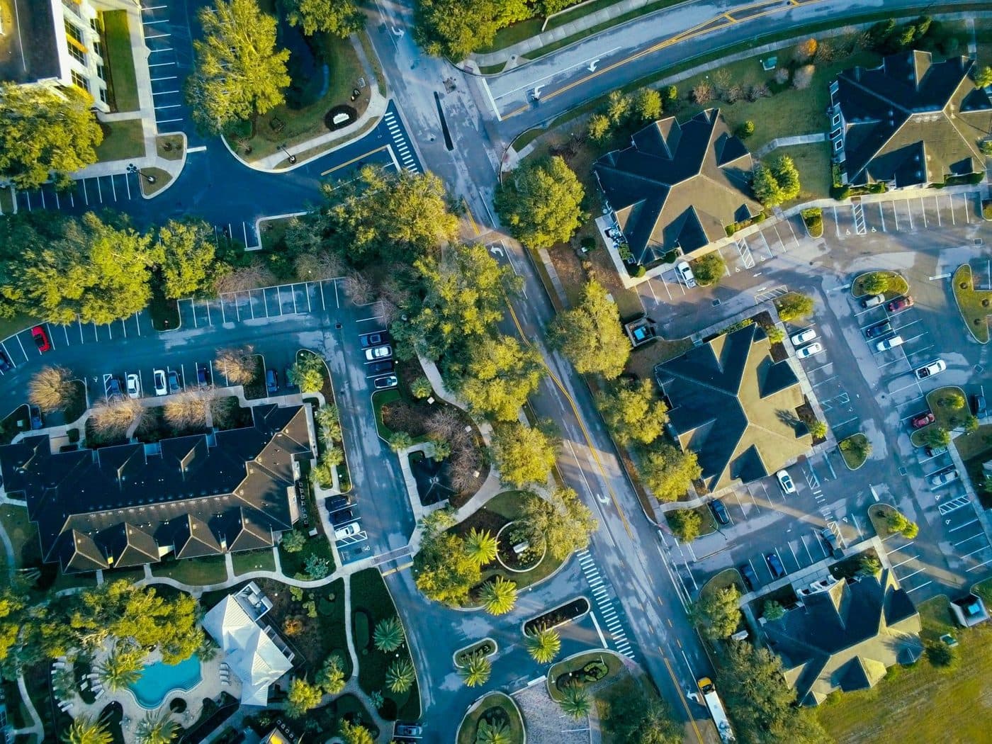 Top-down aerial view of a Florida residential complex with dark-roofed buildings, parking lots, palm trees and a swimming pool