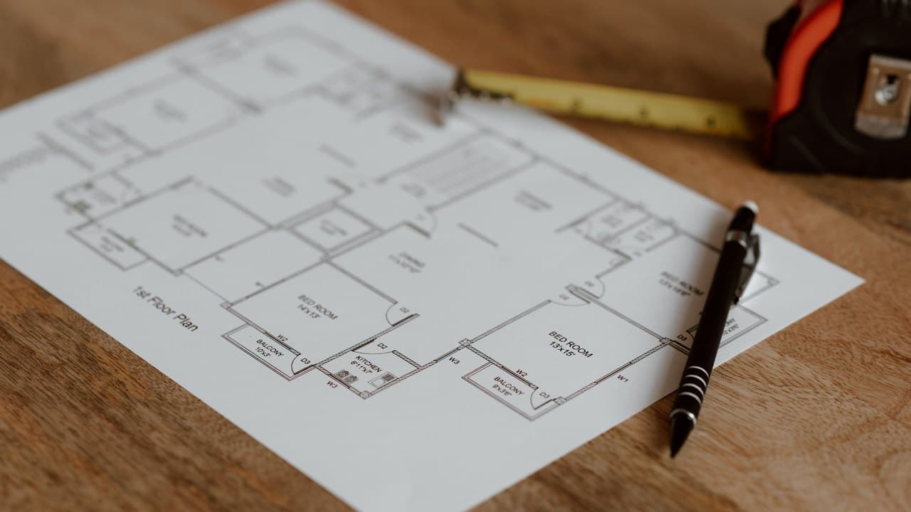 A printed floor plan, pen and tape measure on a wooden bench