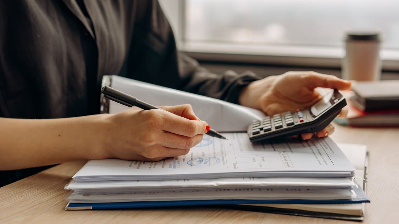 Hands working a calculator over a stack of bound ledgers