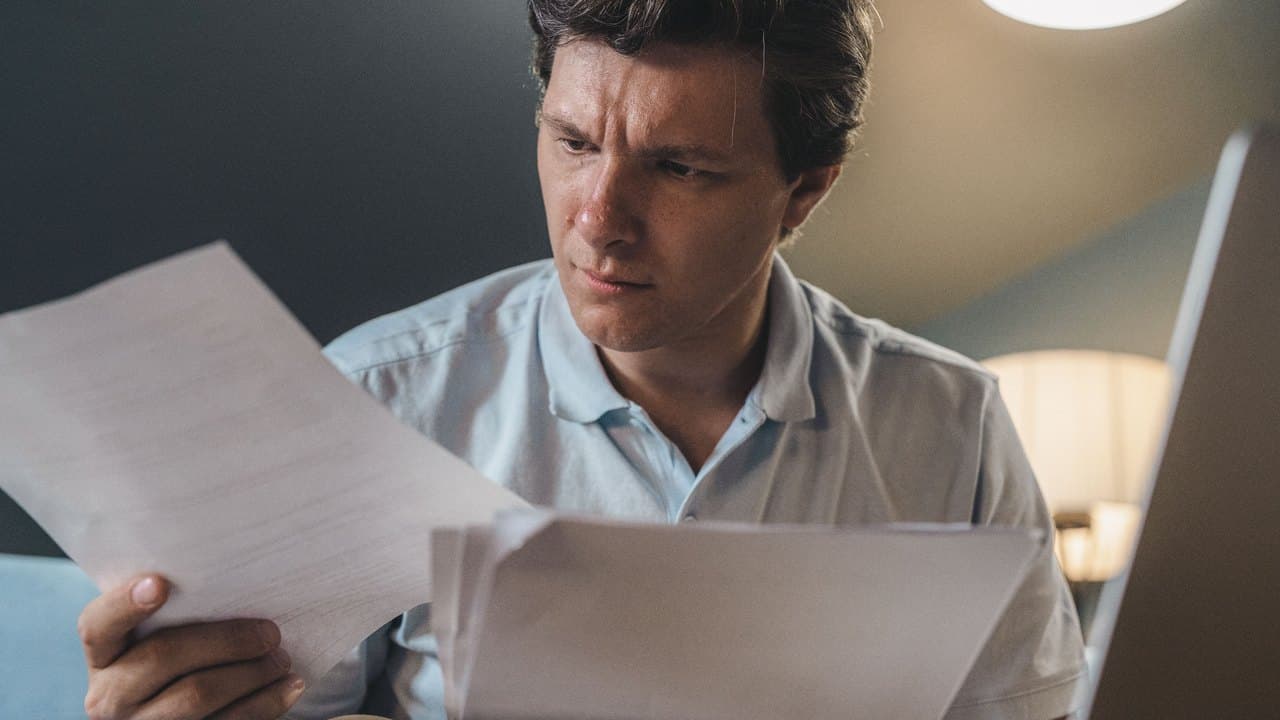 An analyst reading a printed page closely under a desk lamp
