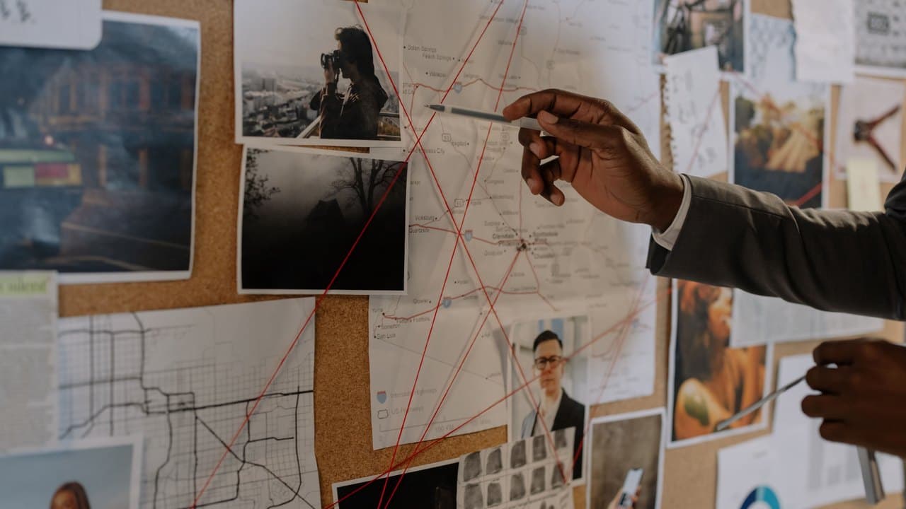 A hand tracing red string between photographs and maps pinned to a corkboard