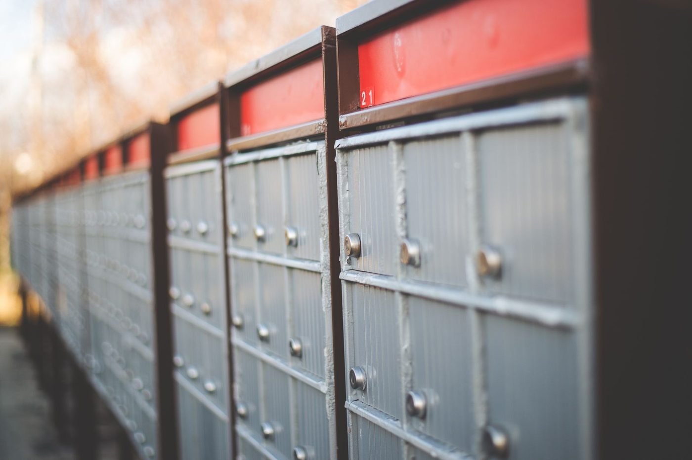 A long row of grey metal post office boxes with red panels above them, receding into the distance
