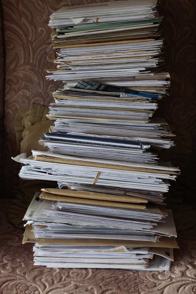 A tall, uneven stack of envelopes, folders and loose papers piled on a patterned upholstered chair