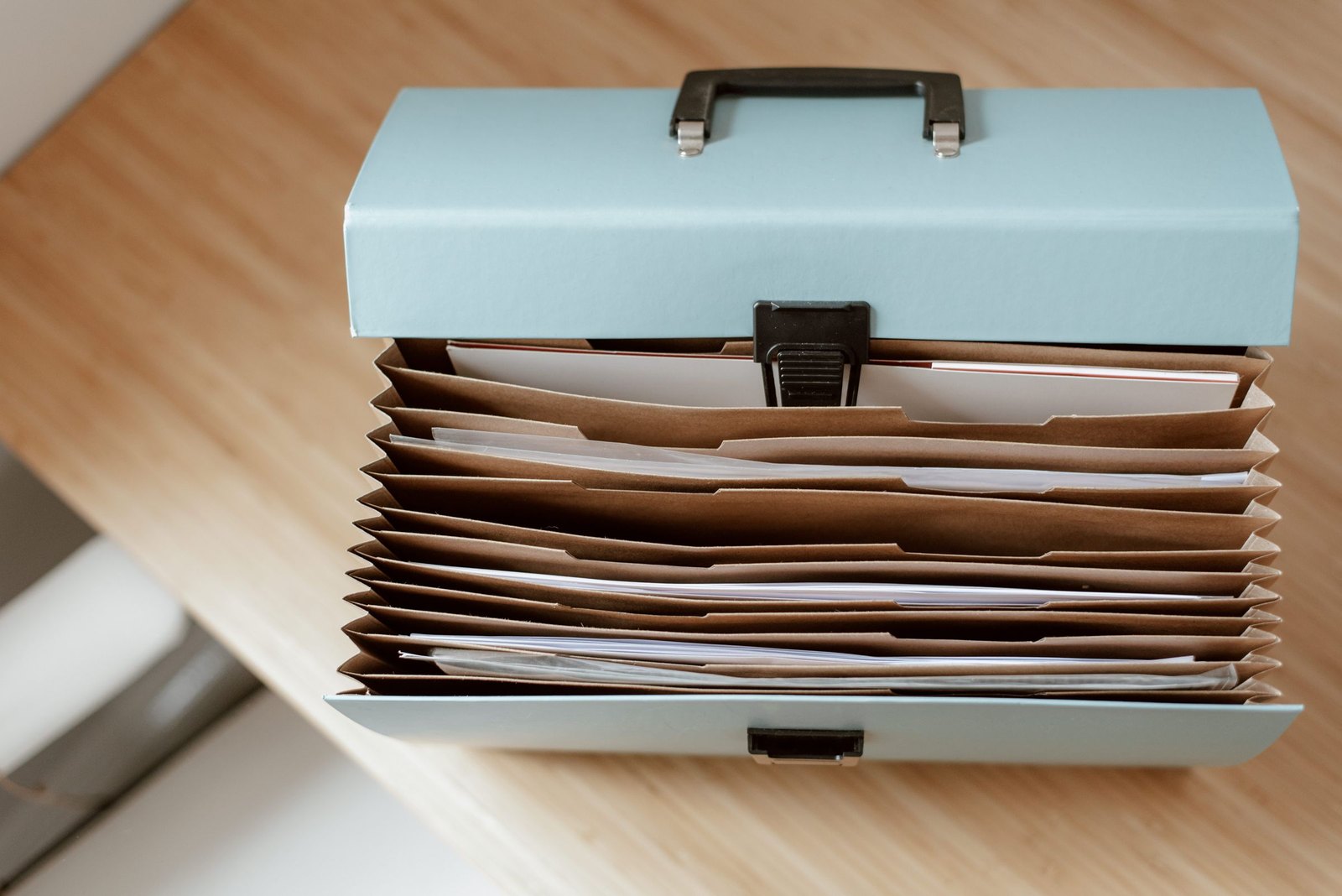 Pale metal file box open on a desk, packed with upright document folders