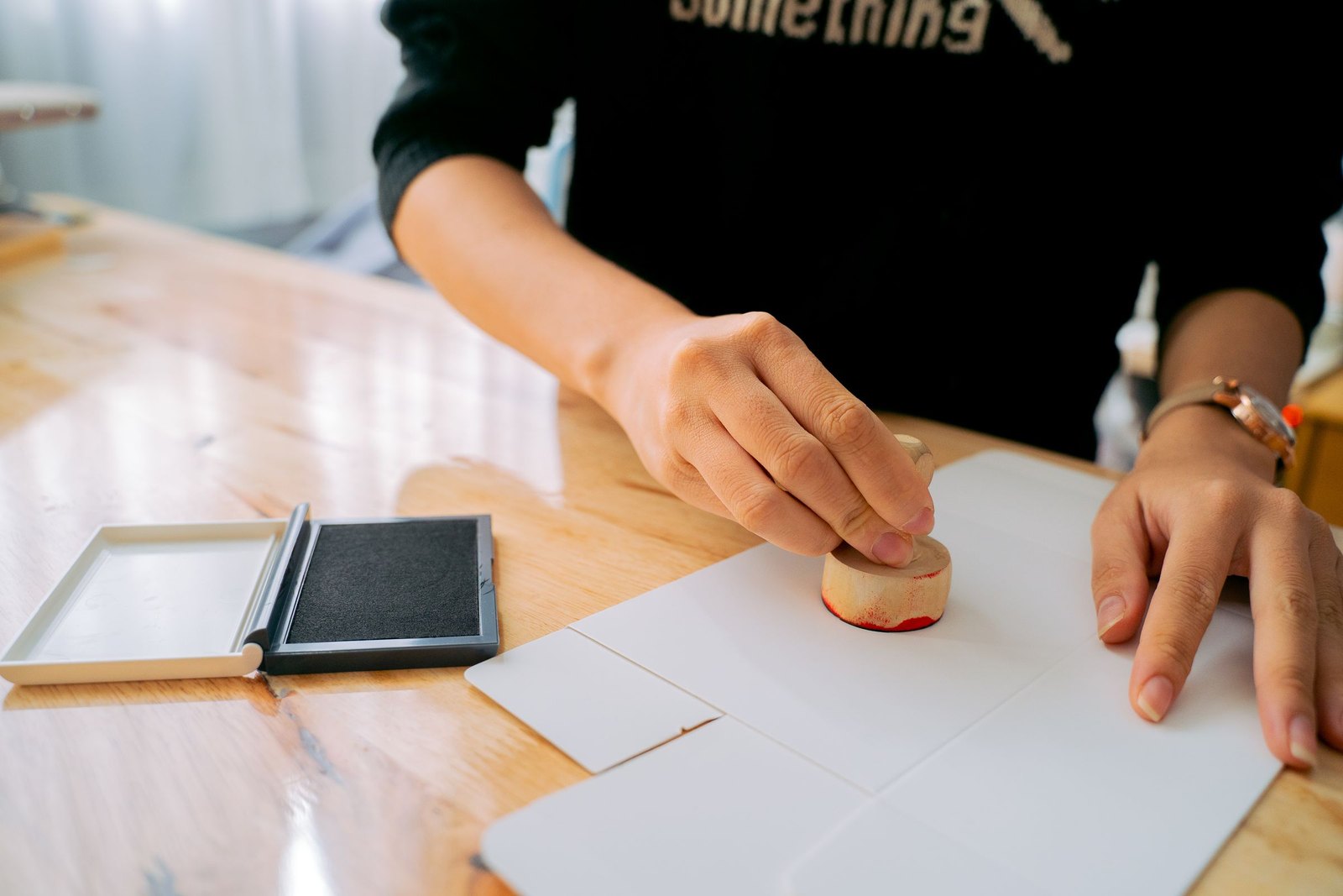 Person pressing a rubber stamp onto a sheet of paper at a wooden desk