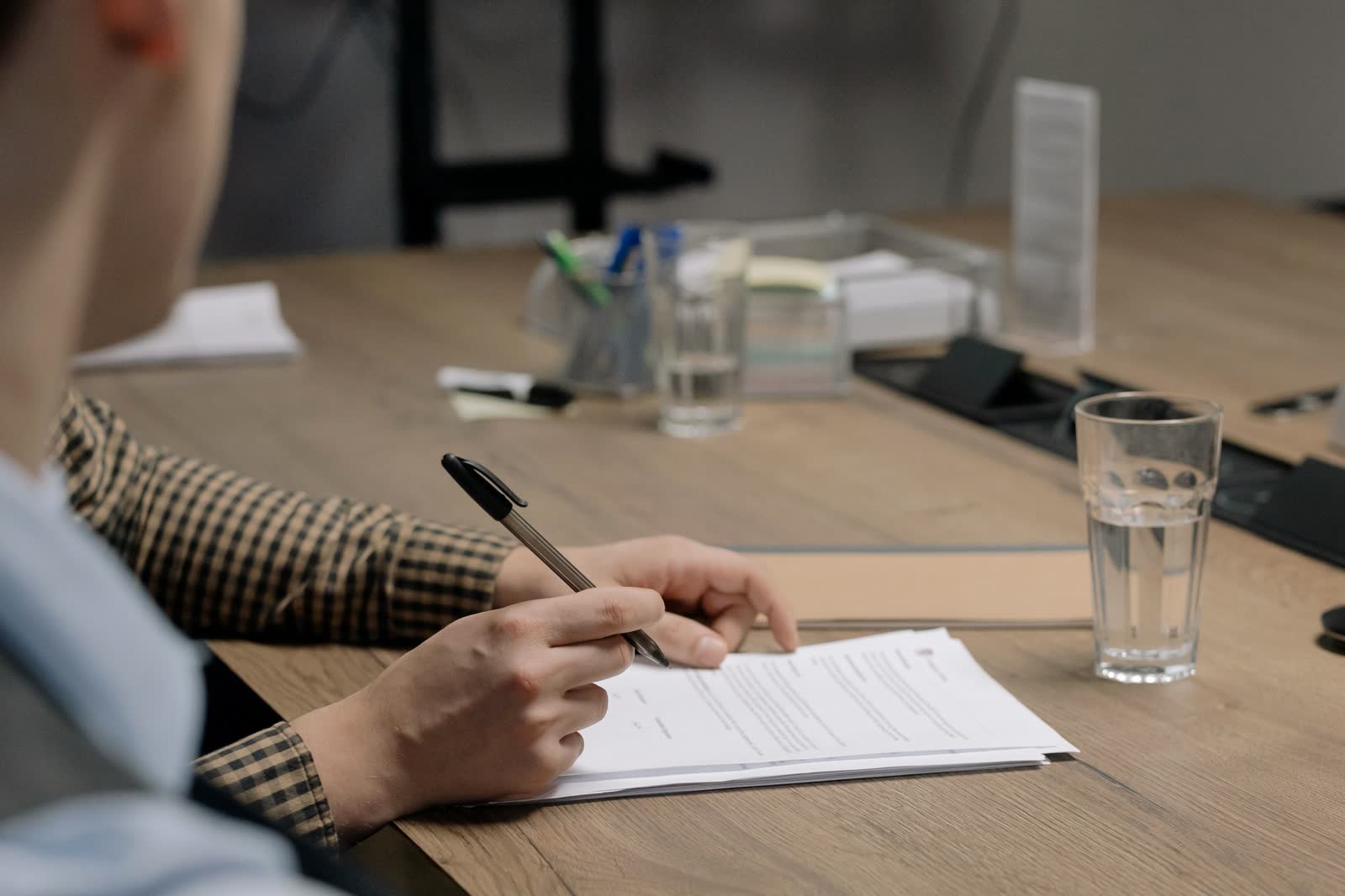 Person marking up a printed document with a pen at a wooden desk