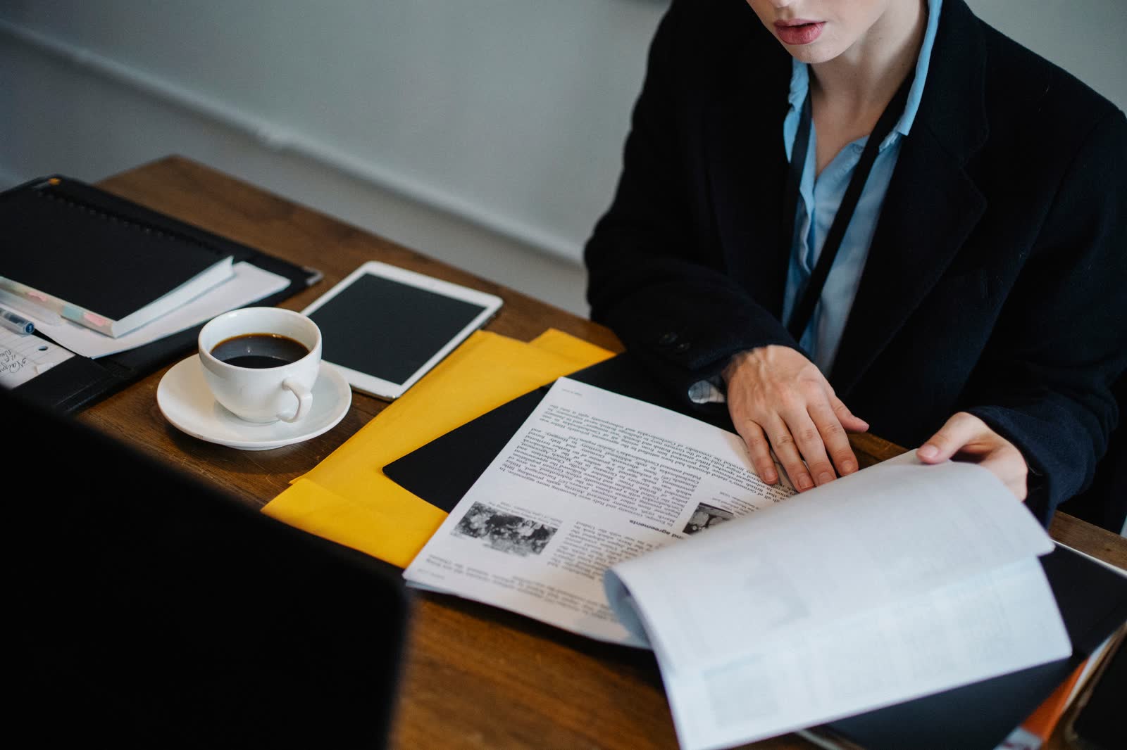 Woman at an office desk reading a printed record beside a coffee cup