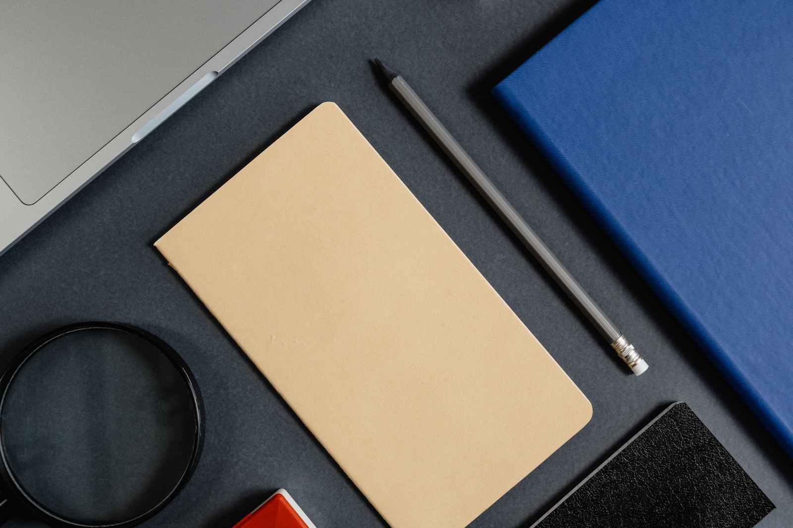Notebook, pencil and lens laid out on a dark blue desk