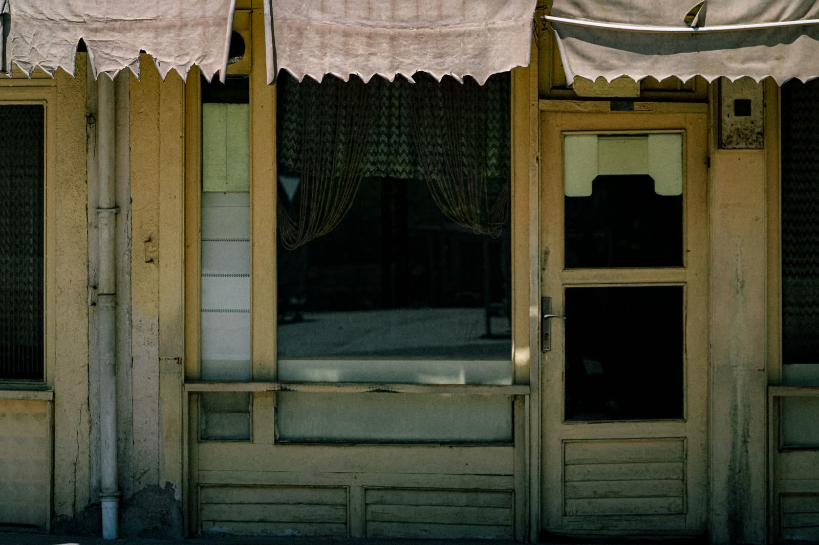 Old shopfront with canvas awnings, a glazed door and no name on the frontage