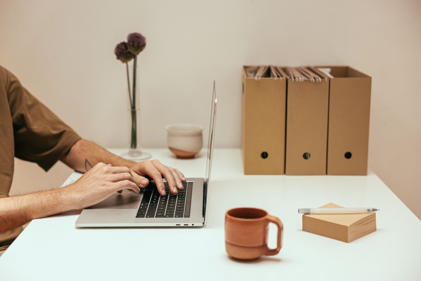 Person working at a laptop on a white desk beside upright archive boxes