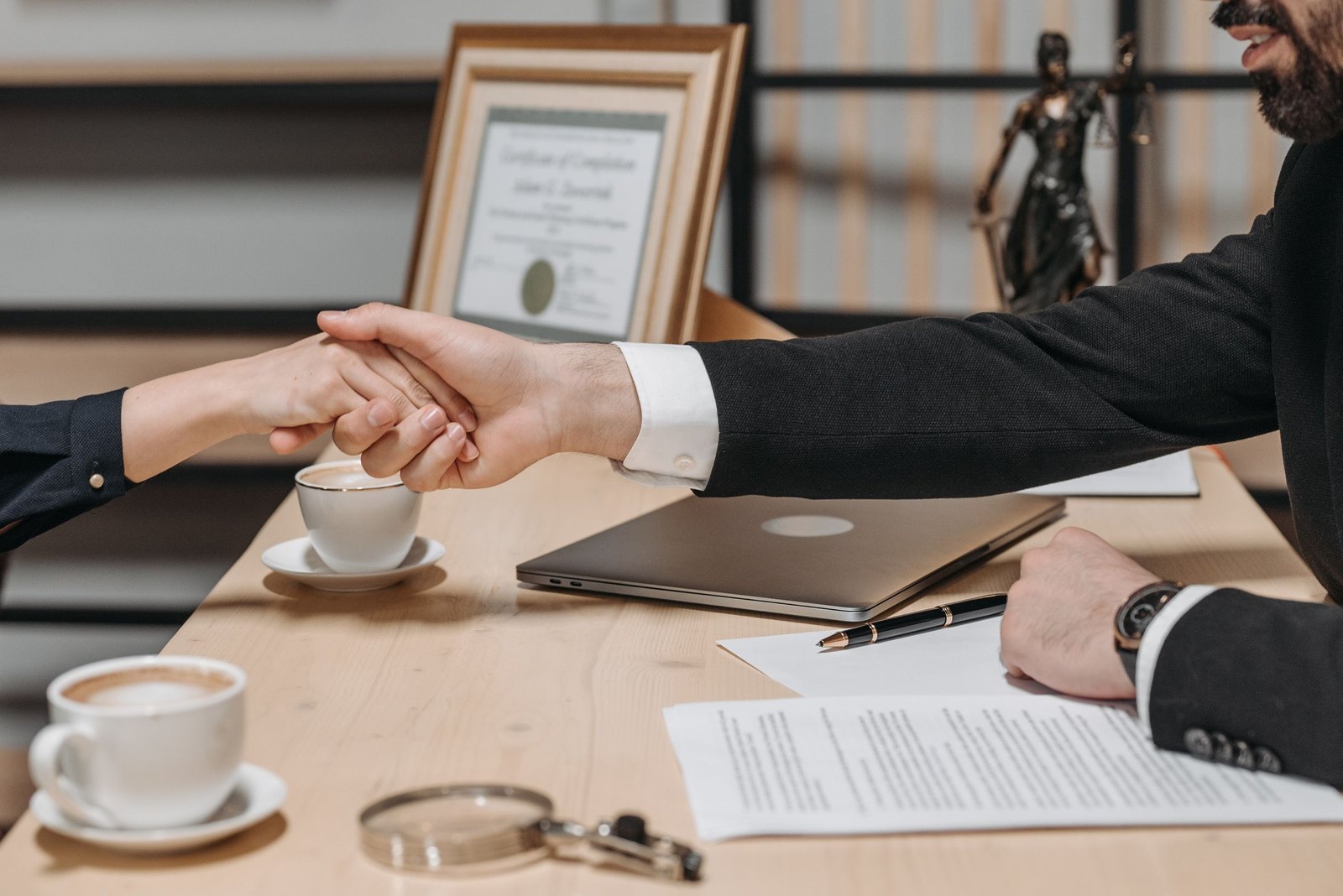 Handshake across an office desk over signed documents and coffee cups