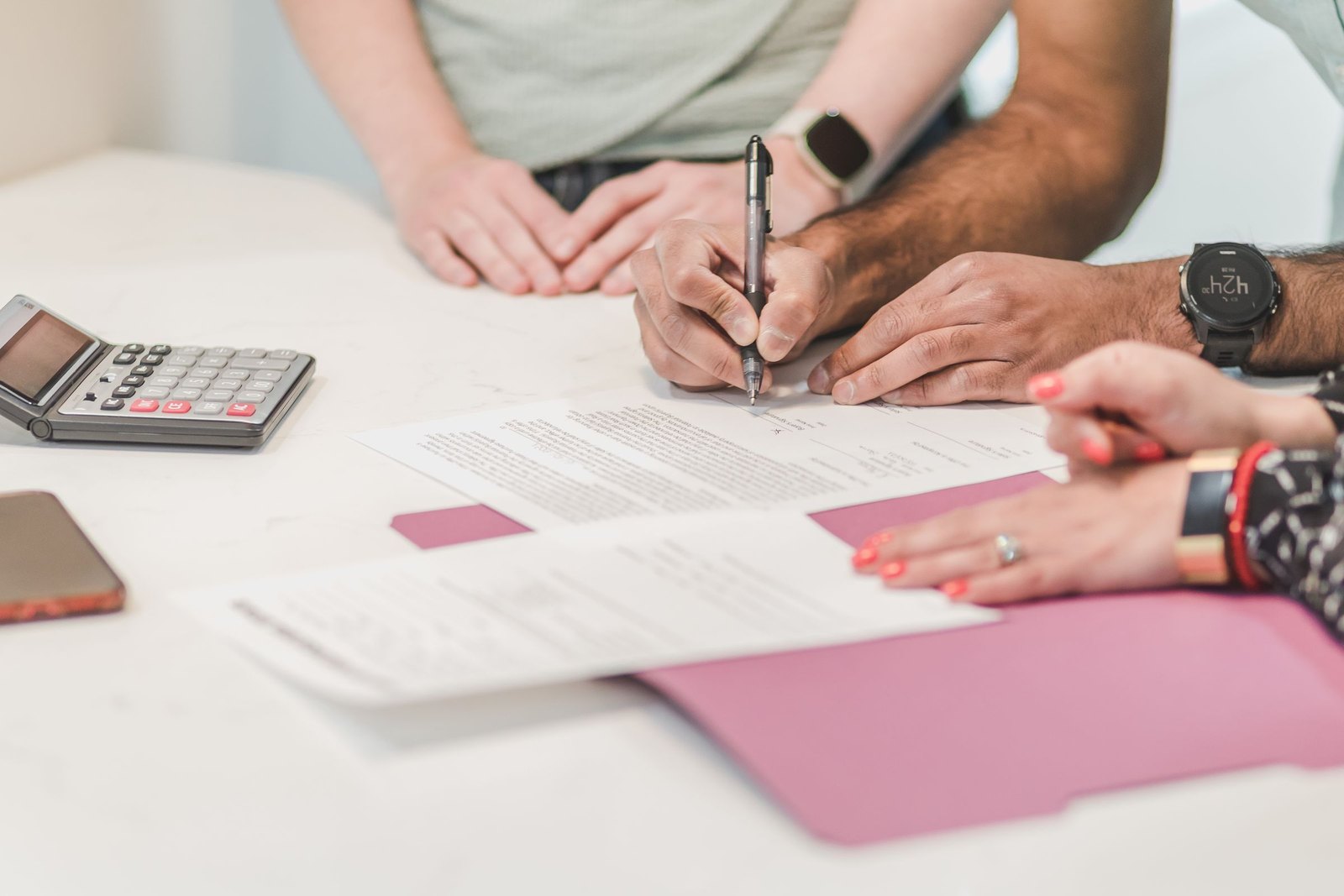 Two people signing paperwork across a desk beside a calculator