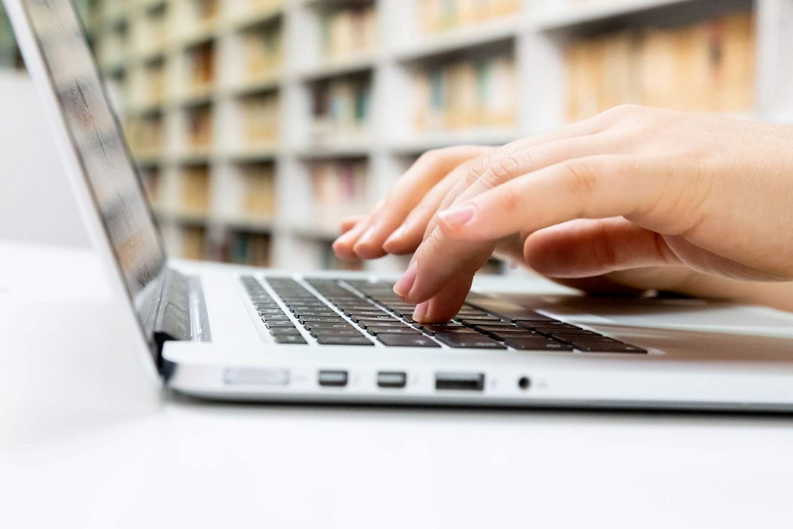 Hands typing on a laptop with library shelves out of focus behind