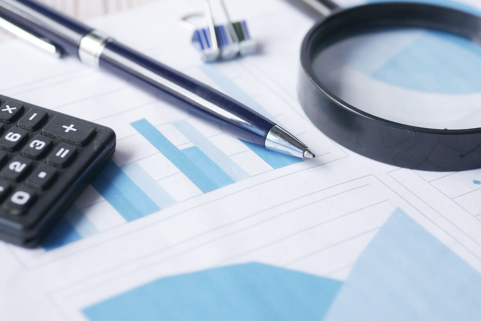 Magnifier, pen and calculator resting on a printed bar chart