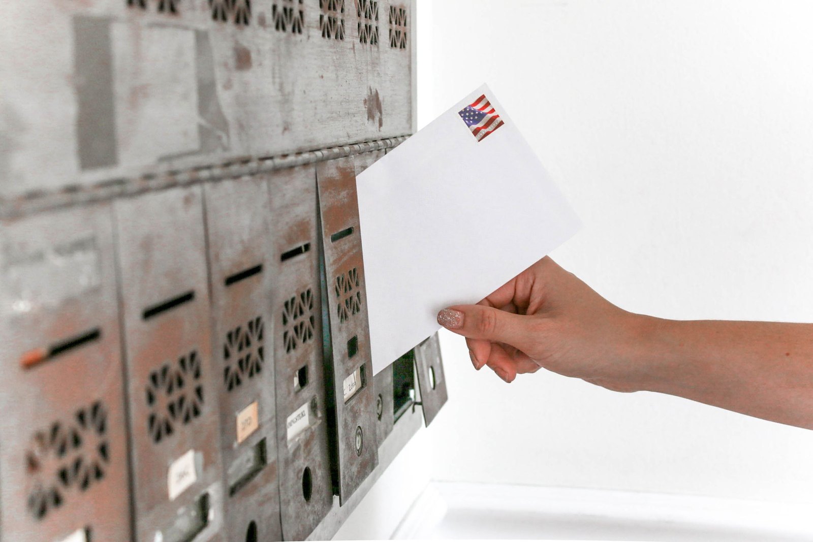 Hand posting a stamped envelope into a bank of metal mailboxes