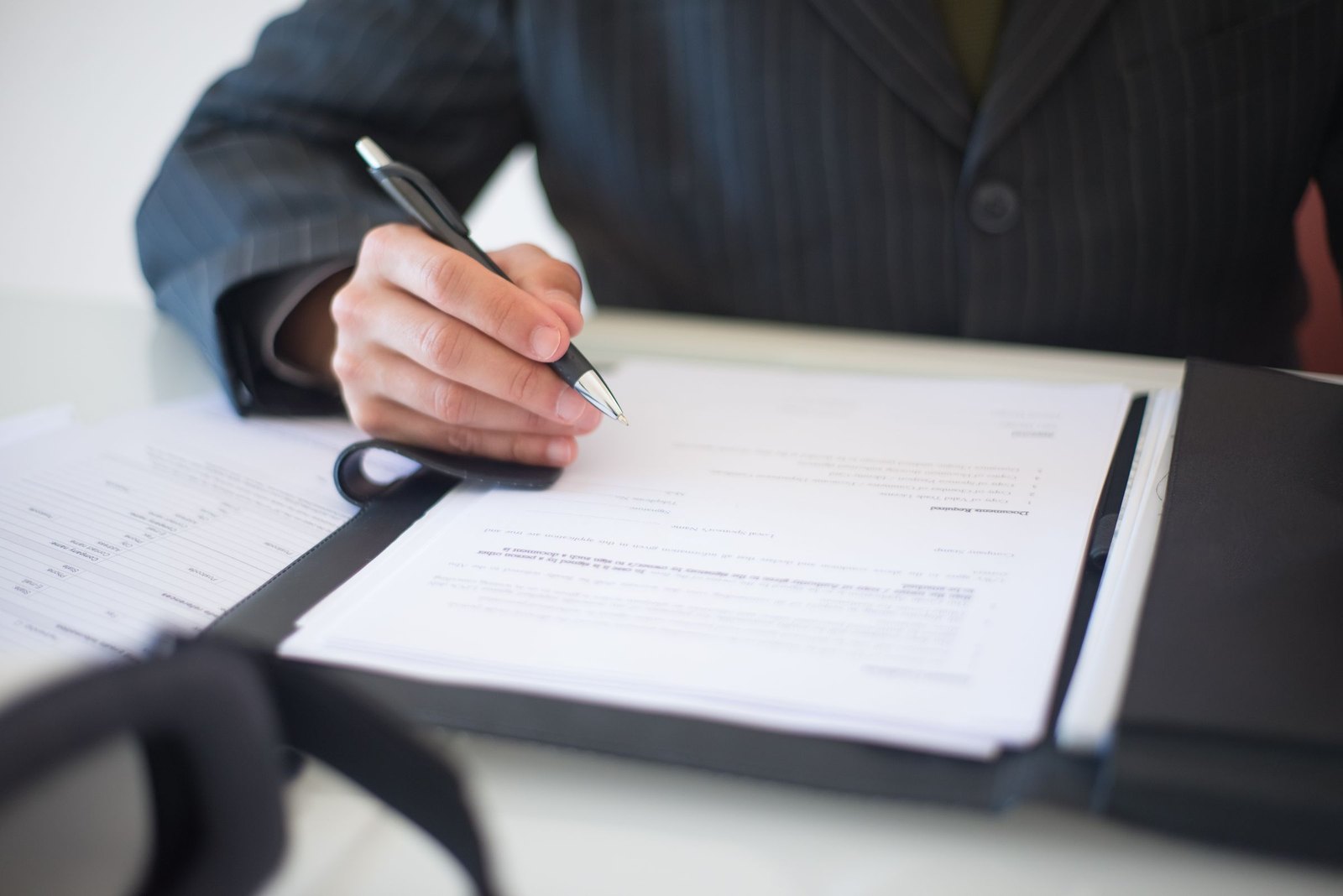 Person signing a printed document in a folder at a white desk