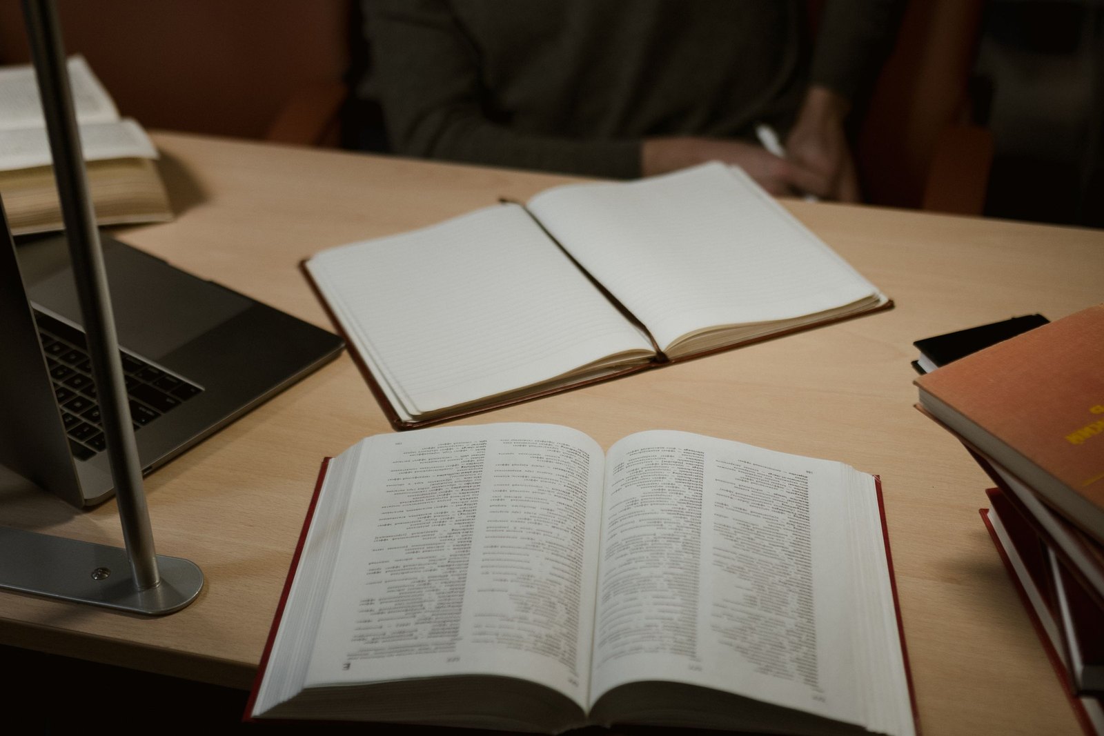 Open reference books and a notebook on a desk beside a laptop