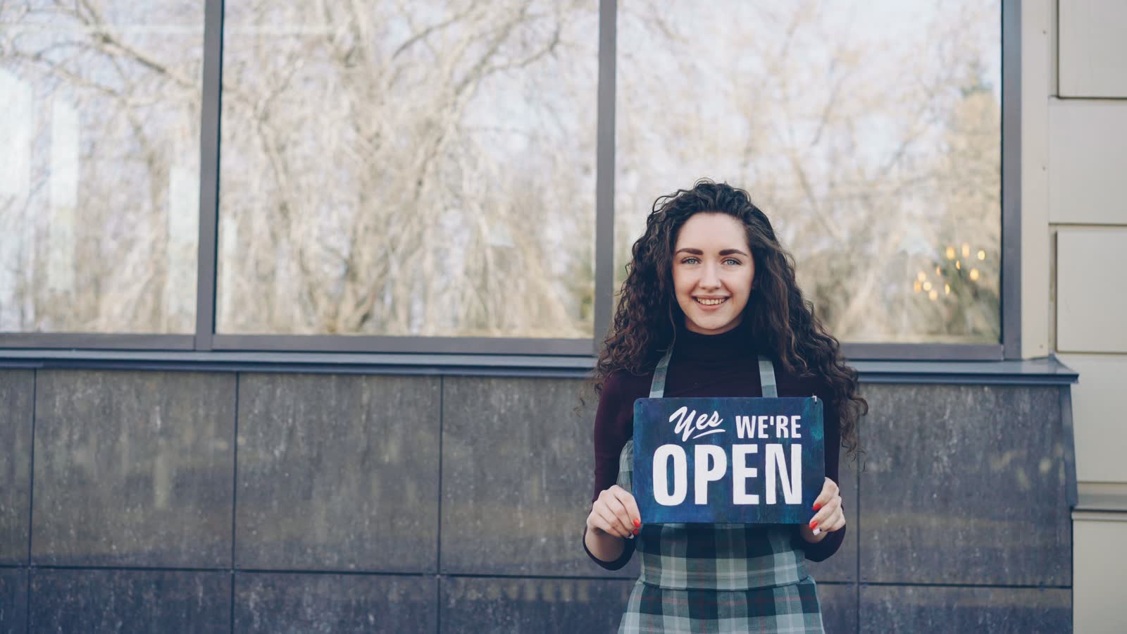 Shop owner standing outside her window holding an open sign