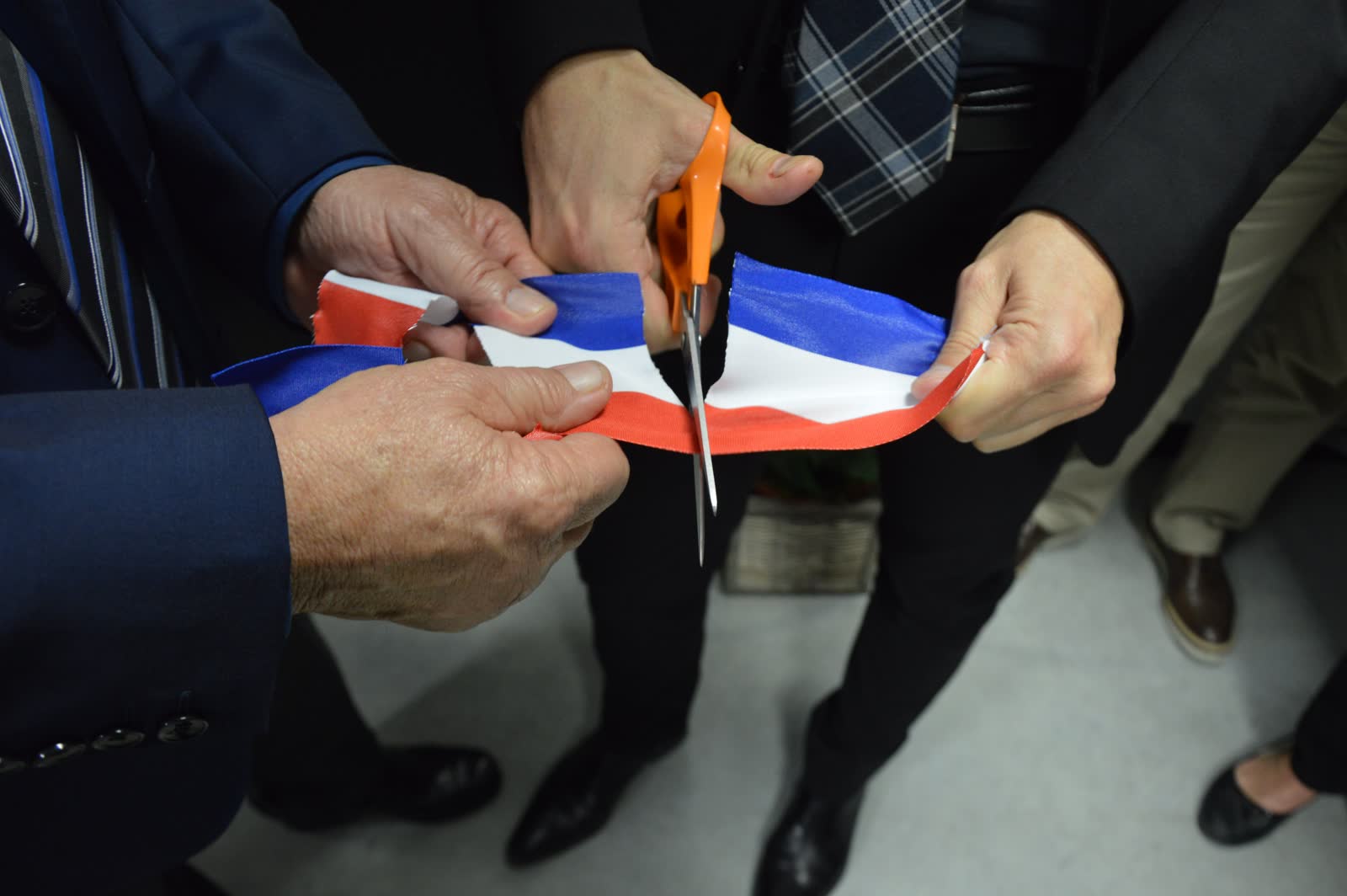 Two people in suits cutting a ceremonial ribbon with oversized scissors