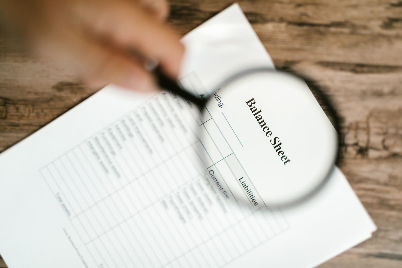 Magnifying glass held over a printed balance sheet